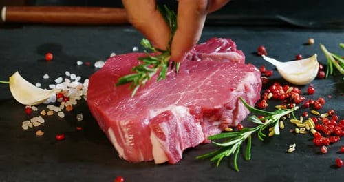 Raw Steak Garnished With Rosemary On Dark Slate