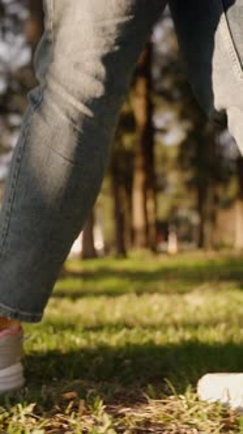 Vertical video. In Slow Motion, Close-Up of Sneaker-Clad Feet Walking on Grass in the Forest.