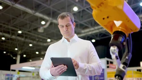Engineer Man Using Tablet at Industrial Robot Robotic Arm Technology in Manufacturing and