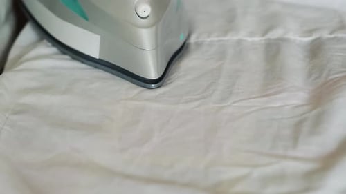 Female Hand Holding Electric Iron Ironing Clothes on Ironing Board
