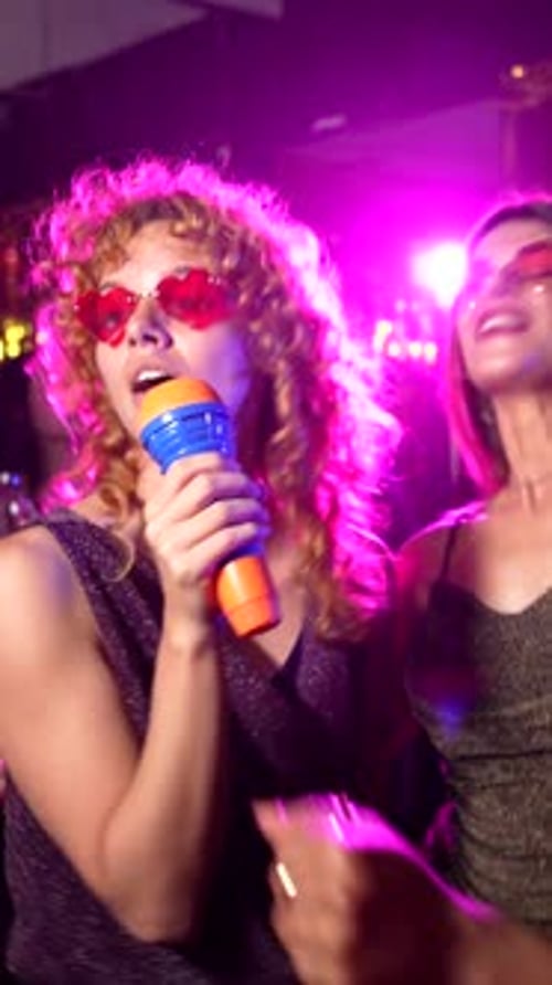Happy Young Women Singing Karaoke in Nightclub