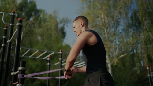 Focused Young Man Working Out in Outdoor Gym on Sunny Day