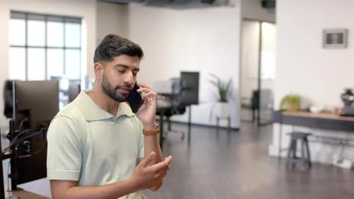 Talking on smartphone, man gesturing while standing in modern office space, copy space