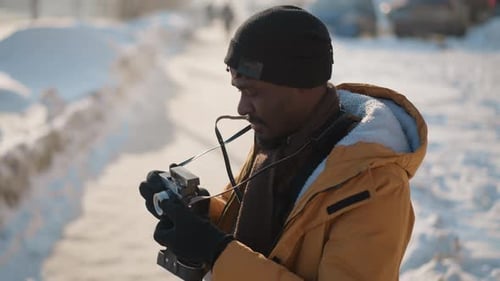 Photographe à angle élevé ajustant la sangle de l'appareil photo sur un trottoir urbain enneigé