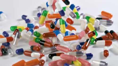 Pills fall onto a white surface in slow motion