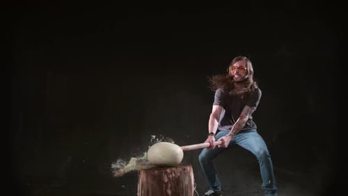 Man Smashes White Ball with Sledgehammer on Wood Stump