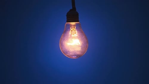 Incandescent Lamp Glows and Flickers on Dark Blue Background Place for Text