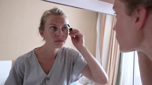 Beautiful woman making up by the mirror in hotel room