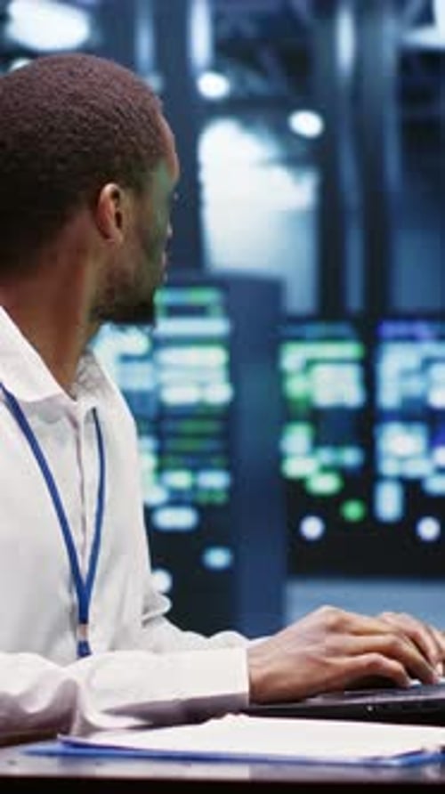 Young Adult Typing on Laptop in Server Room
