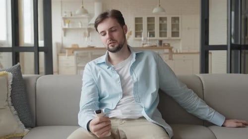 Man Sitting on Couch Watching Television with Remote