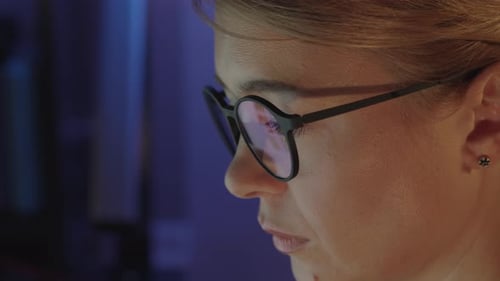 Female eyes in eyeglasses late at night scrolling in front of laptop. Woman coder, programmer