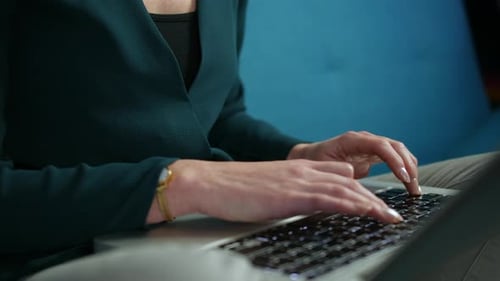 Close up of an unrecognizable woman working, typing on a laptop keyboard while sitting on a sofa