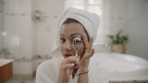 Woman Curling Eyelashes in White Bathroom