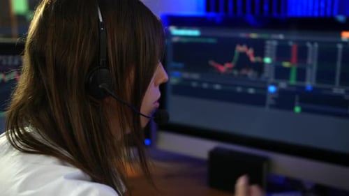Female stock trader analyst talking to client wearing headset microphone looking at graphs