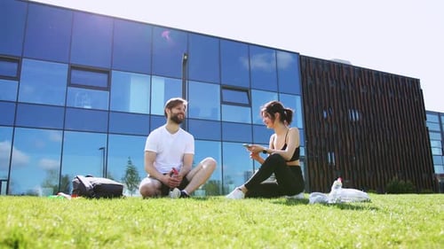 Athletic Couple Sitting on Lawn Drinking Water