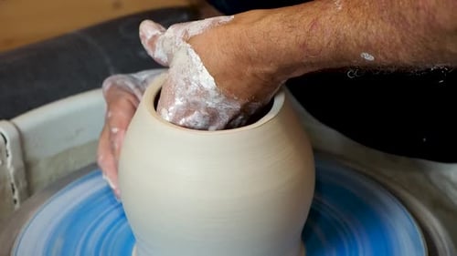 Close up of the potter's hand shaping and molding clay on a turning wheel .