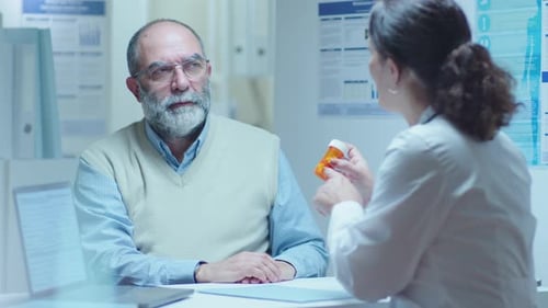 Female Doctor Giving Pills to Senior Male Patient in Clinic