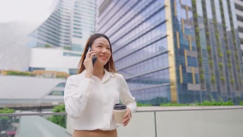 Asian young businesswoman talking on smartphone while standing in city.