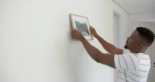 Man Hanging Picture on Wall in Bright Home