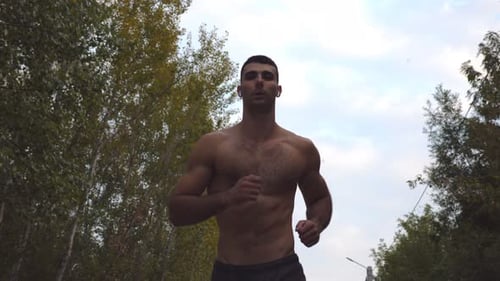 Handsome Sporty Man with Wireless Headphones Running Along Road with Beautiful Nature Landscape at