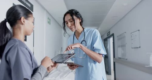 Diverse doctor and nurse using tablet and talking in corridor at hospital, in slow motion