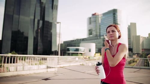 Young Woman with Earphones on Bridge Outdoors in City, Resting After Exercise