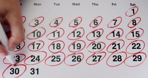 Junge Frau kreist alle Daten auf einem Monats-Papierkalender mit roter Markierung in Nahaufnahme