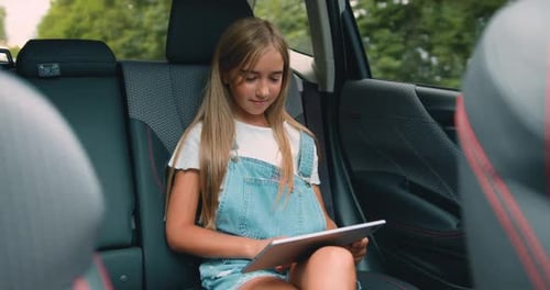 Une petite fille attachante dans une voiture lisant une tablette numérique et regardant Dessins animés en ligne.