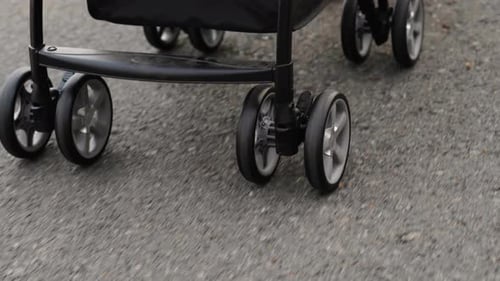 close up wheel of baby stroller with woman pushing and walking on the pathway