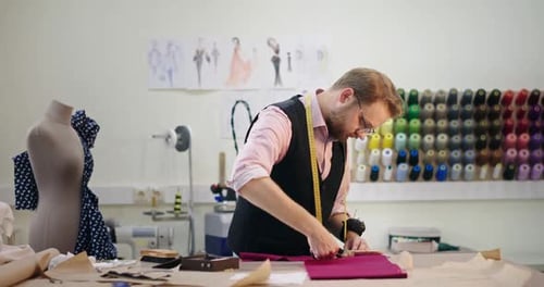 Man Tailor with Measure Tape Cuts Purple Fabric in Studio
