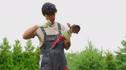 Young Man Builder Carpenter Repairs a Grinding Machine in the Backyard