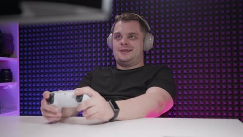 Gamer Sits at Table and Plays Console in Studio Enthusiastic Man with Joystick in His Hands Plays
