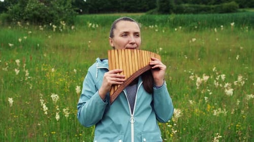 Una joven toca la flauta de pan en la naturaleza