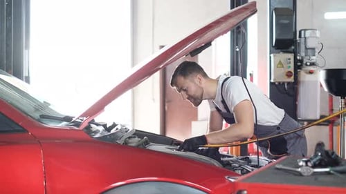 A Professional Car Mechanic Examines a Car at a Car Service Performing a Series of Tests