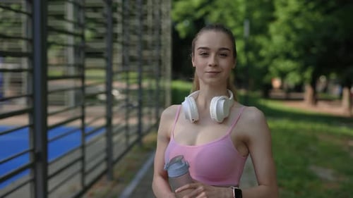 Athletic Woman Outdoors with Headphones and Water Bottle