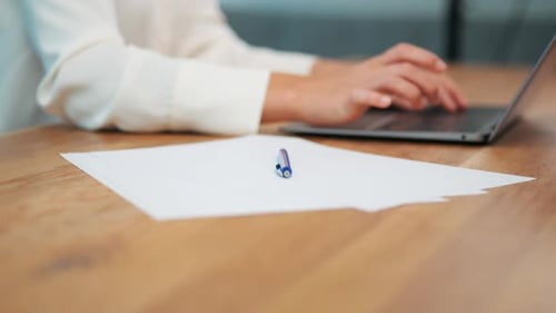 Blank white paper on wooden desk next to businesswoman working on laptop