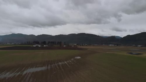 Flying over Farmland wet fields of crops rows of vegetables on farm in country valley surrounded by