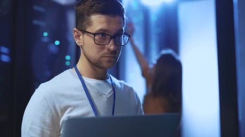 Technician Using Laptop in Data Center with Server Racks