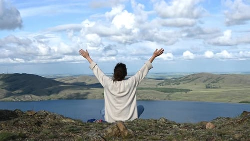 Woman Sitting on the Edge of the Cliff and Raising Hands