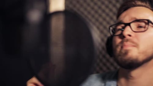 Male singer with headphones singing song at sound recording studio session