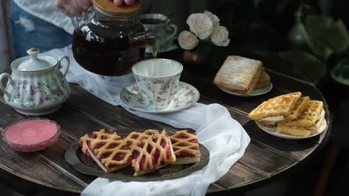 Woman Pours Tea With Pastries on Table