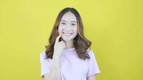 Asiatisches Mädchen trägt lässiges rosa T-Shirt auf gelbem Hintergrund.