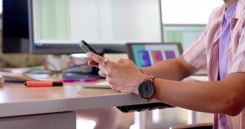 Midsection of asian male creative using smartphone at desk in casual office, slow motion