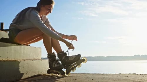 Beautiful Young Girl Puts on Roller Skates in Skate Park