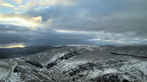 Snowy mountain landscape with clouds and sunlight peeking through, aerial view