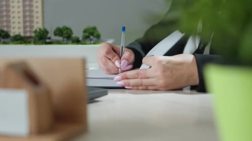 Close Up of Woman Writing Beside House Miniature in Office Workspace