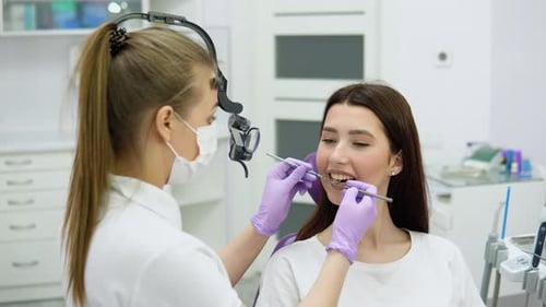 Female Dentist Examining Young Girl Looking on the Teeth with Professional Microscope in the Surgery