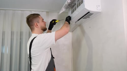 Man Repairs Air Conditioner Unit on the Wall