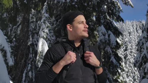 Young Man With Backpack Hikes In The Mountain With Snowy Forest On A Sunny Day. - medium shot