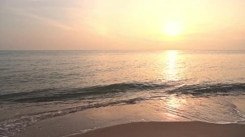 Stunning sunset over calm sea with little waves rolling onto a sandy beach. Golden hour light reflec